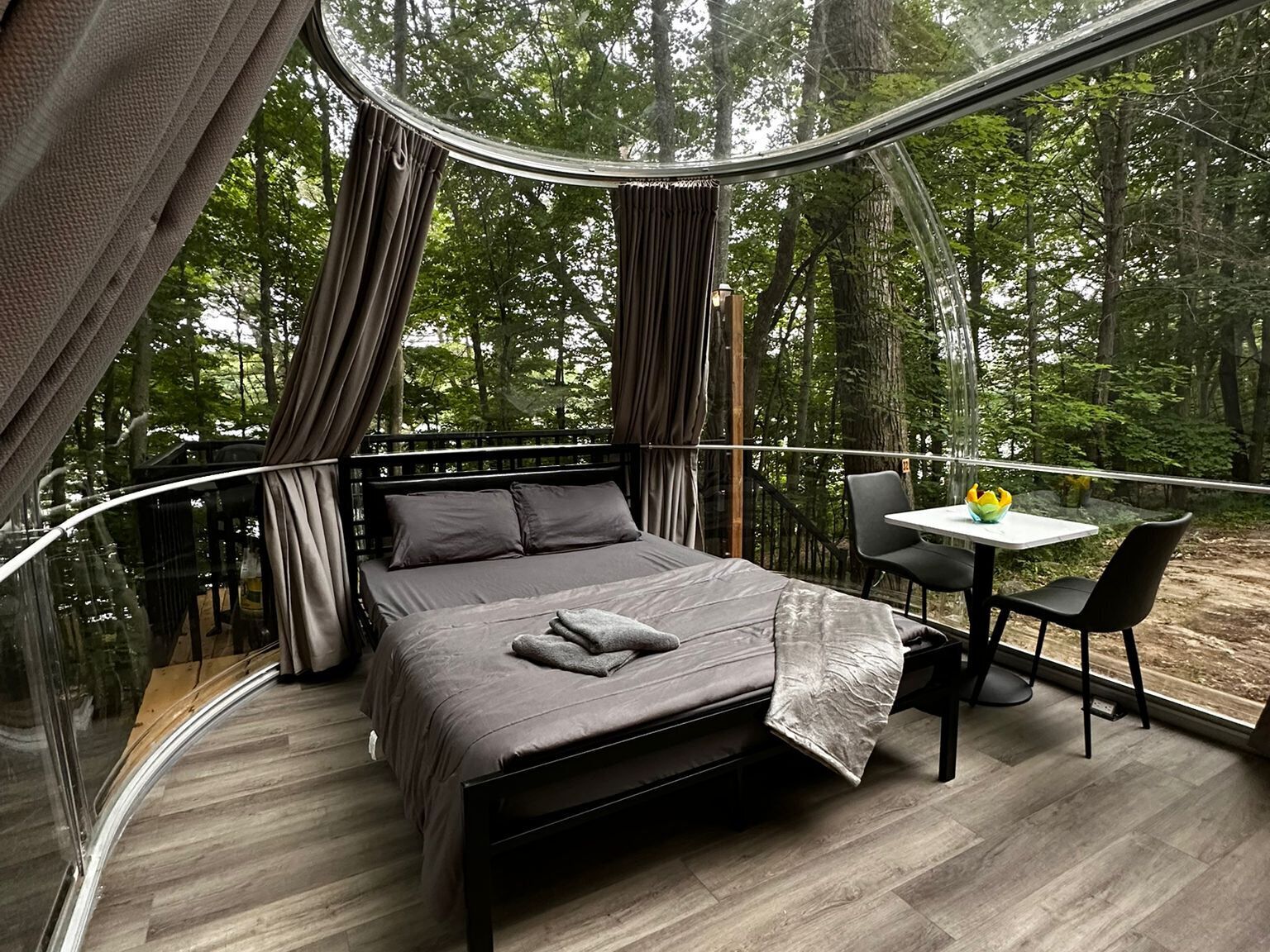 A bedroom with a curved glass wall, a bed, a table, and chairs.
