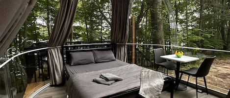 A bedroom with a curved glass wall, a bed, a table, and chairs.