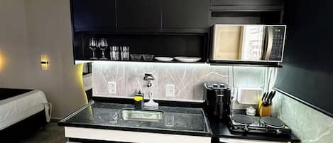 Cocina compacta con microondas, lavamanos y cafetera.