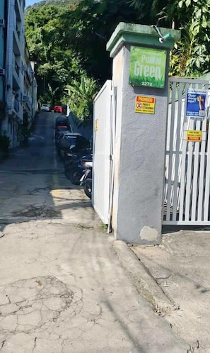 Entrada com portão e placa verde indicando caixa postal, sinalização de estacionamento e código QR para aplicativo móvel.