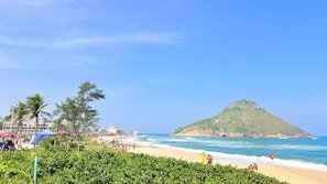 Ein Strand mit einem Hügel im Hintergrund, Sonnenschirmen und Menschen.