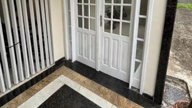 Een witte deur met glaspanelen, een hal met zwart-beige tegels en een metalen poort aan de linkerkant.