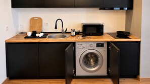 A compact kitchen with a built-in washing machine, a microwave, and a sink. - Mikado Lounge – 2BR by Freedom Square with Fireplace (T'bilisi)