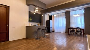 A modern kitchen with a built-in refrigerator, a dining area with a table and chairs, and a bar area with stools. - Mikado Lounge – 2BR by Freedom Square with Fireplace (T'bilisi)
