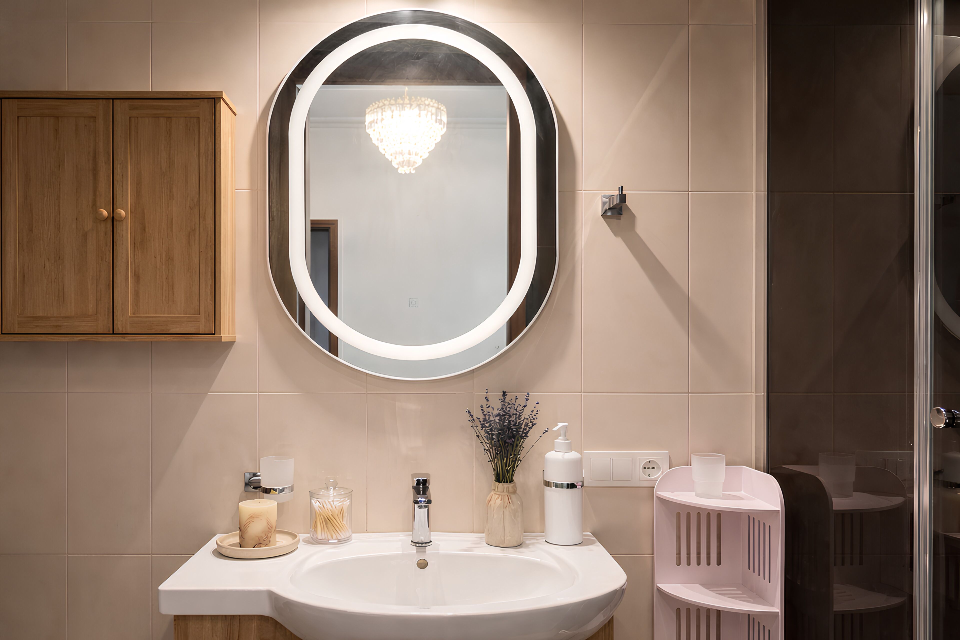 Une salle de bain avec un lavabo blanc, un miroir avec éclairage intégré, un meuble en bois et une cabine de douche en verre.