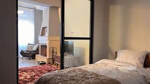 A bedroom with a bed, a sofa, a fireplace, and a view of a balcony. - Mikado Lounge – 2BR by Freedom Square with Fireplace (T'bilisi)