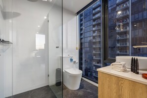 Un baño moderno con cabina de ducha de vidrio, inodoro blanco y tocador con lavamanos y toallas apiladas.