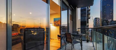 A balcony with a sofa, chairs, and a table, overlooking a cityscape at dusk.