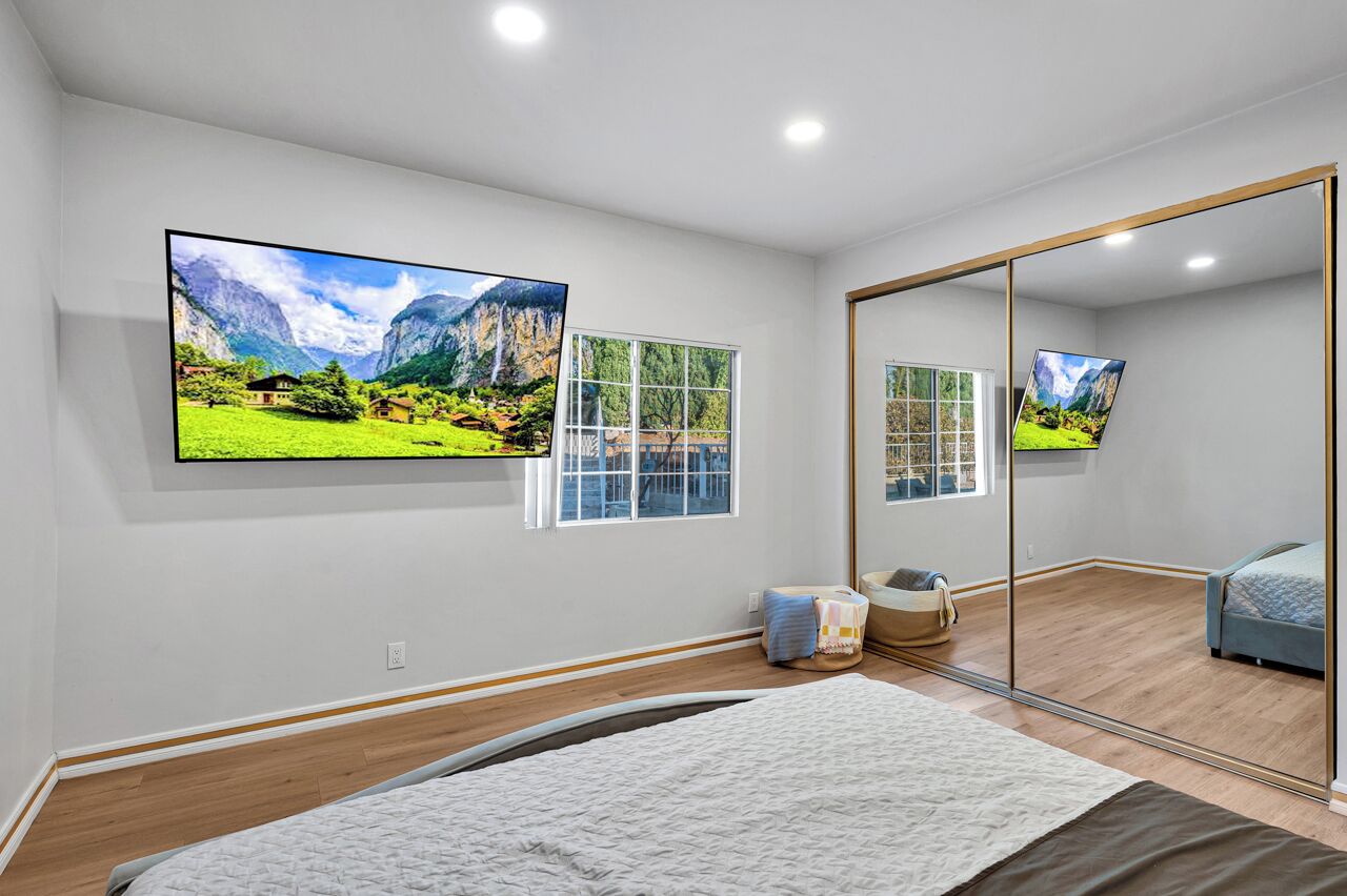 Una camera da letto con un letto, un grande specchio e due televisori a parete che mostrano paesaggi suggestivi.