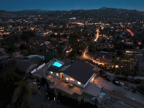 Vue aérienne d’un quartier résidentiel au crépuscule, avec des maisons, une piscine et une route sinueuse.
