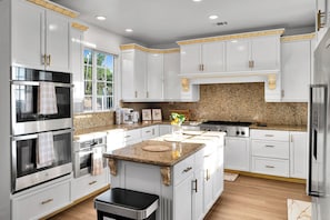 Une cuisine moderne avec des meubles blancs, des plans de travail en granit, des appareils électroménagers en acier inoxydable et un îlot central.