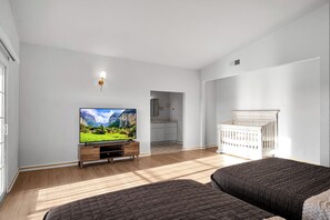 Quarto com televisão, berço e vista para uma cozinha e banheiro.