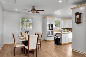 Cozinha moderna com armários brancos, uma ilha central e uma área de jantar com mesa e cadeiras de vidro.