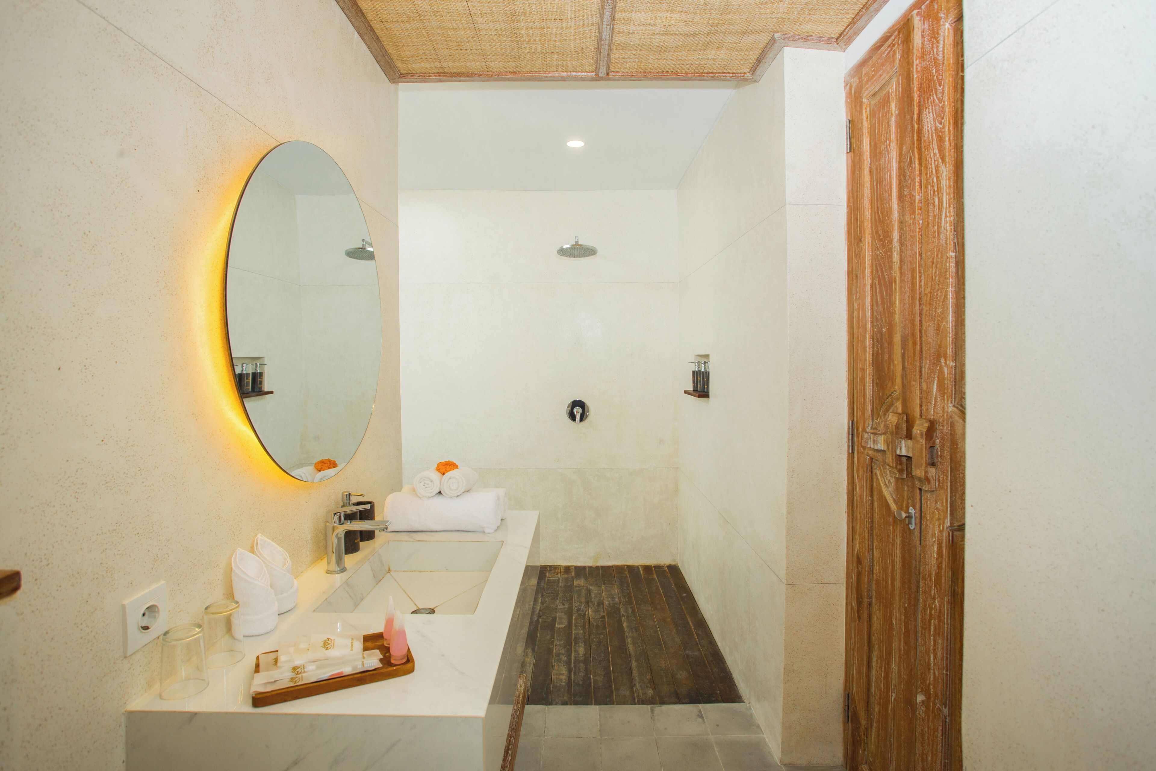 A bathroom with a large mirror, a sink, a shower, and a wooden door.