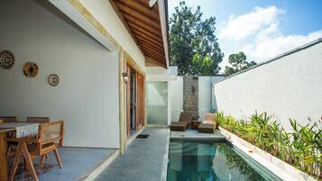 Un área de piscina con mesa y sillas, una pared de piedra y vista a árboles.