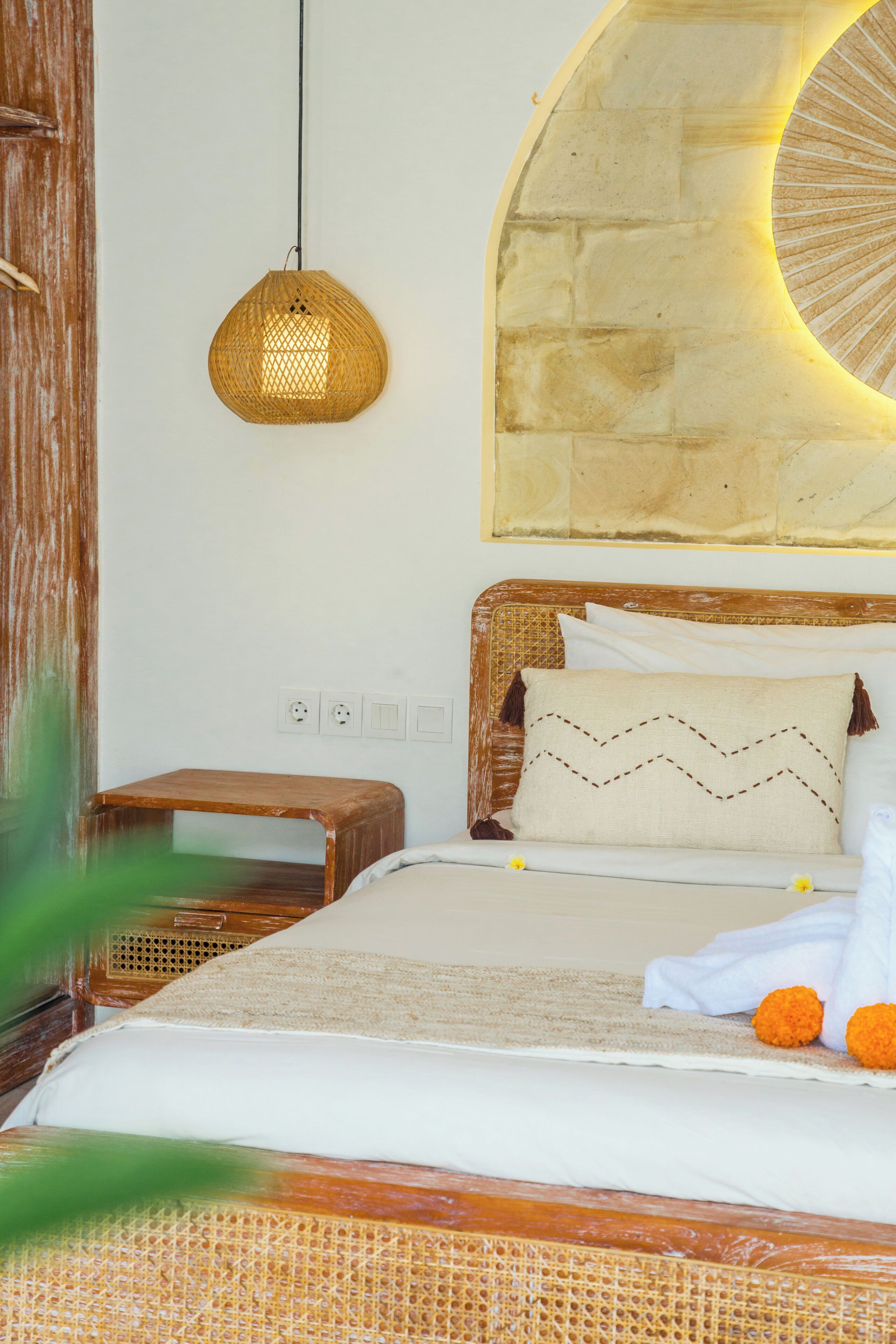 A bed with a headboard, a bedside table, a wall-mounted light fixture, and a wall with a circular design.
