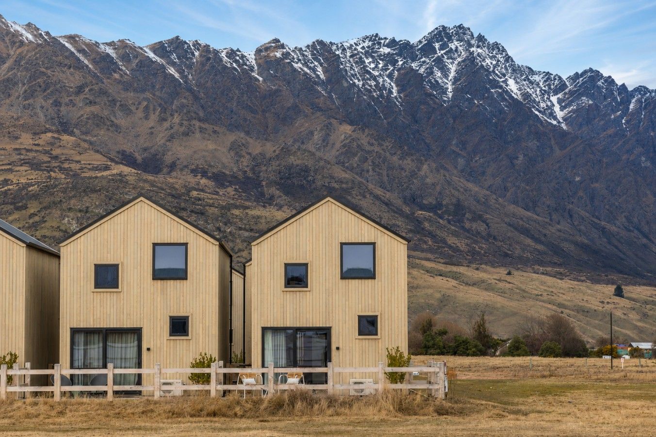 A row of wooden cabins with large windows, set against a backdrop of mountains.