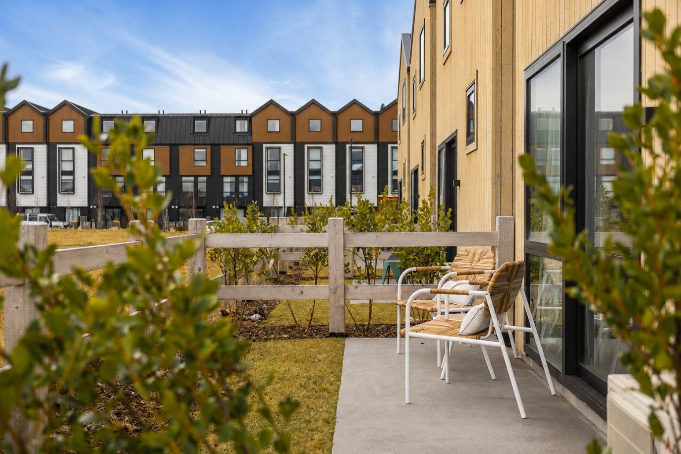 Une rangée d’immeubles résidentiels modernes, avec une clôture en bois et un espace extérieur aménagé avec des sièges.