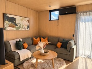 A modern living room with a grey sofa, orange cushions, a round coffee table with a vase, and a painting on the wall.