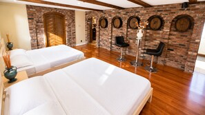 Habitación de hotel con dos camas, una pared de ladrillo con ventanas circulares y piso de madera.