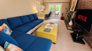 Una sala de estar con un sofá azul, un reposapiés amarillo, un televisor de pantalla plana y una chimenea.
