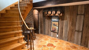 Una escalera de madera con barandilla de metal que conduce a una habitación con piso de piedra y paredes de madera.