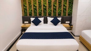 A hotel room with a bed, a bedside table with a phone, a trash bin, and a wall with vertical greenery.