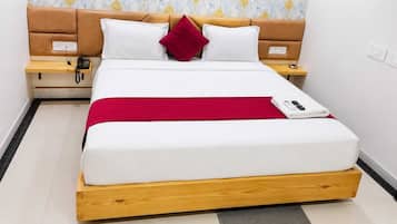 Una cama bien tendida con una manta roja, una mesita de noche con un teléfono y otra mesita con una lámpara.