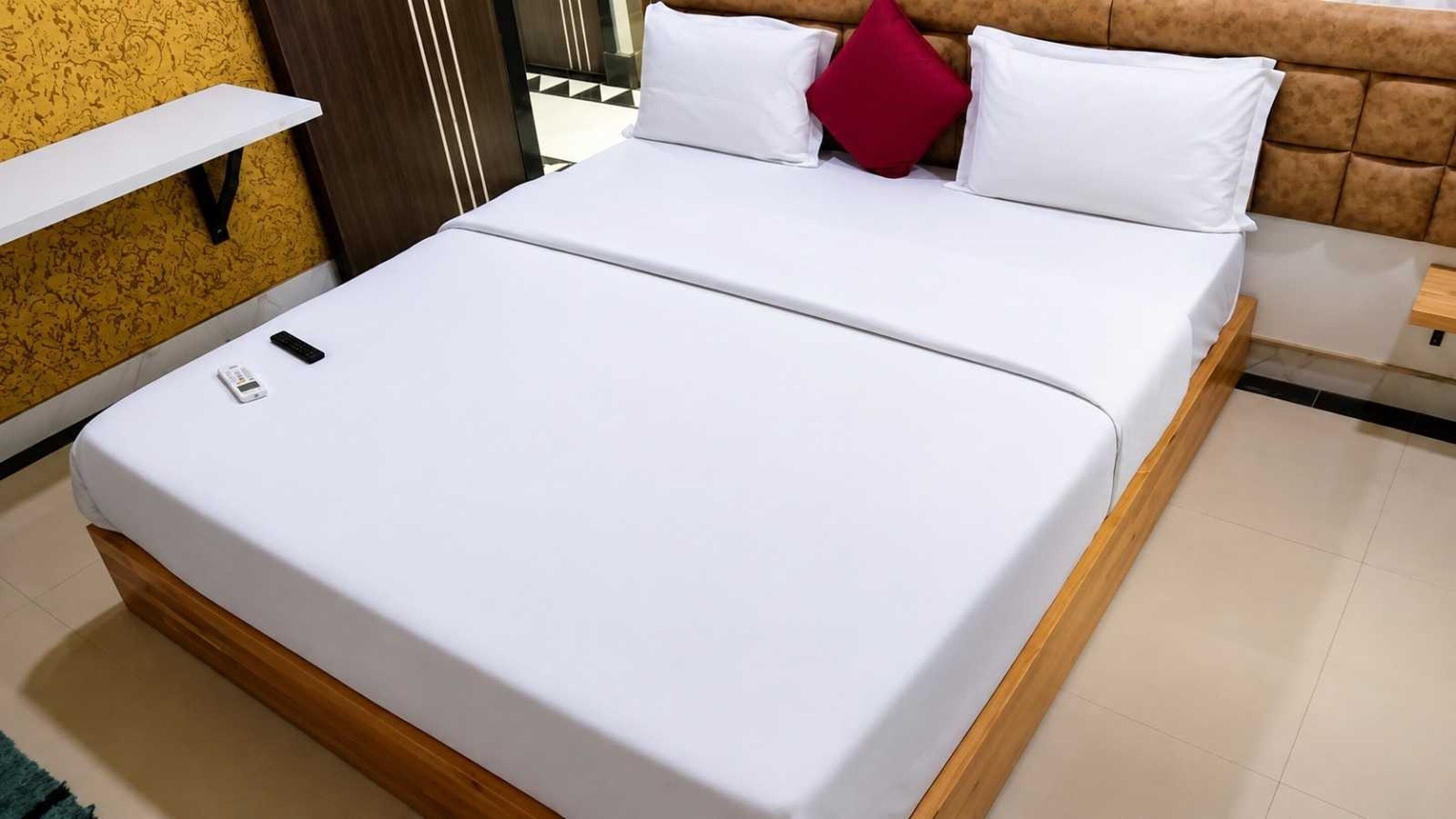 A bed with a white mattress, a wooden headboard, and a red pillow.