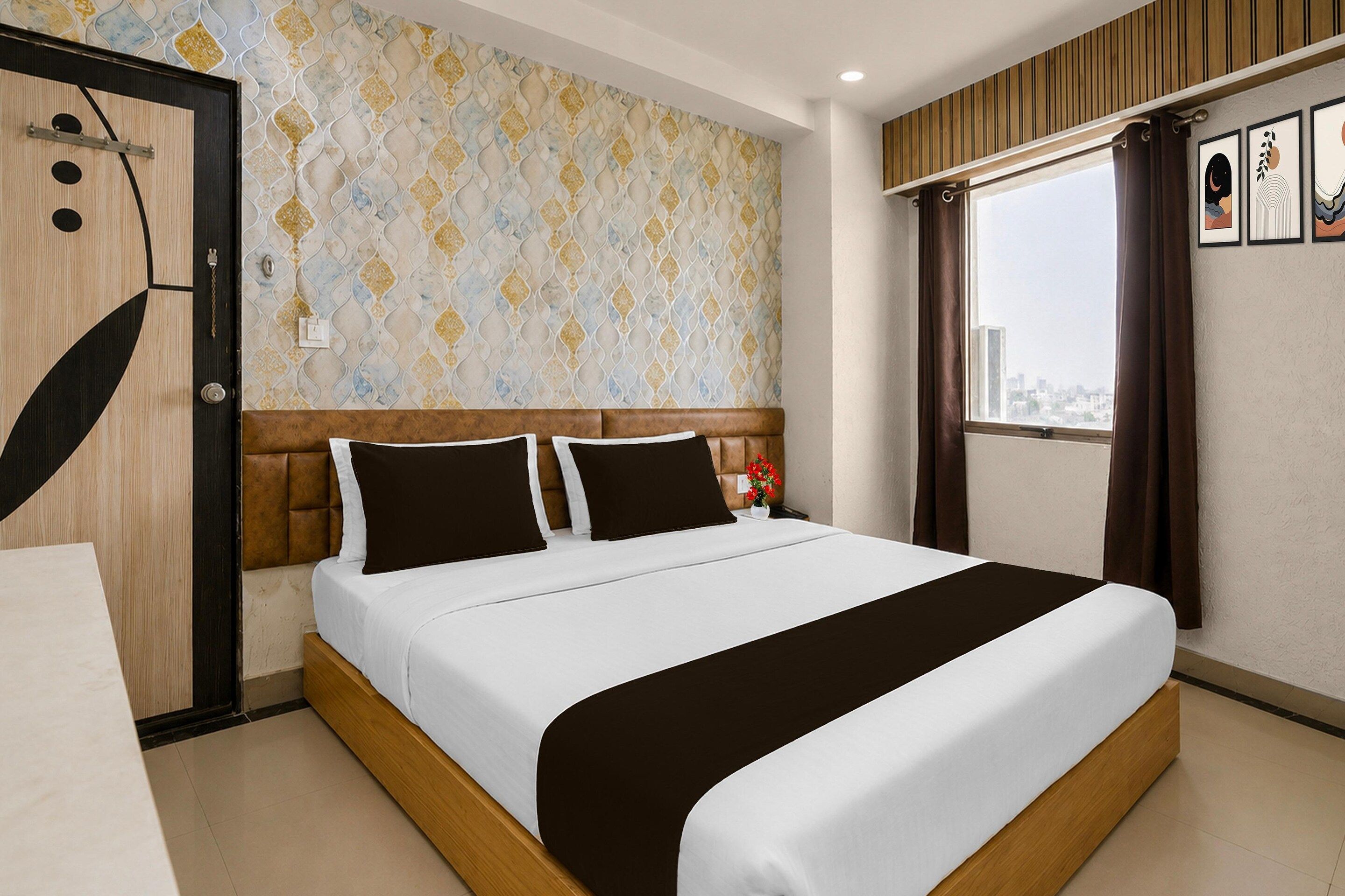 A hotel room with a bed, a window with curtains, a wall with patterned wallpaper, and a door with a handle.