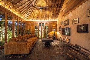 A spacious living area with a wooden ceiling, a sofa set, a coffee table, and a TV mounted on the wall. - Rahasia Rumah Kerang Uluwatu (Pecatu)