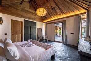 Een slaapkamer met een groot bed, houten plafond en uitzicht op een buitenruimte.