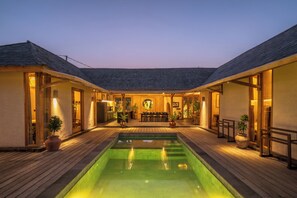 A pool area with a wooden deck, a dining table, and potted plants. - Rahasia Rumah Kerang Uluwatu (Pecatu)