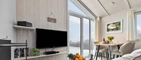 Una sala moderna con televisor de pantalla plana, estanterías de madera, una mesita con fruta y un balcón con vistas.