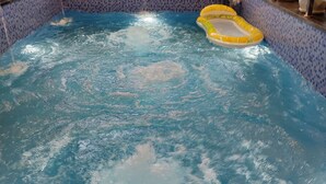 An indoor swimming pool with a tiled wall, a window, and a small inflatable pool. - Shubh Ashray (UDAIPUR)