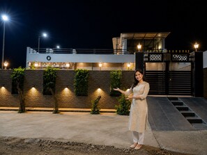 A person standing in front of a modern building with a gated entrance, a staircase, and a well-lit facade.
