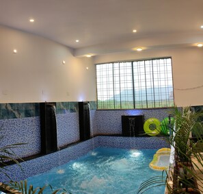 A swimming pool with a tiled wall, a window with a grid pattern, and a ceiling with recessed lighting.