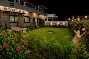 A well-lit outdoor area with a lawn, seating, and a building with multiple air conditioning units.