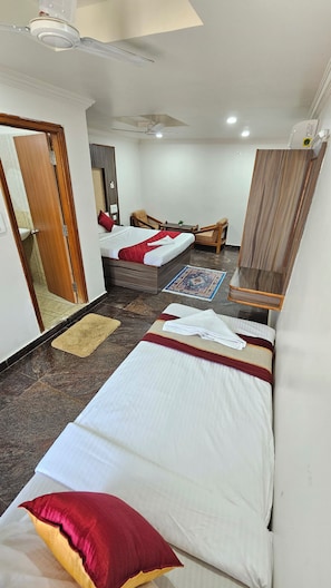Una habitación de hotel con cama, una silla, una mesita, un espejo y un ventilador de techo.