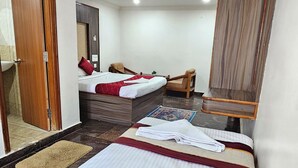 A hotel room with a bed, a desk, a chair, a mirror, and a ceiling fan. - HOTEL SRB SUITES - TPT (Tirupati)