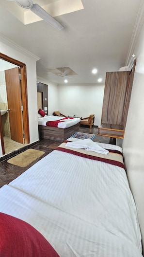 A hotel room with a bed, a desk, a chair, a mirror, and a ceiling fan. - HOTEL SRB SUITES - TPT (Tirupati)