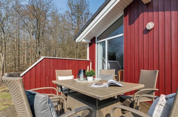 A red building with a large window, wicker furniture, and a table with a magazine. - Holiday Home With 1 Bedroom (Braunlage)