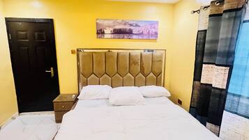 A bedroom with a bed, a headboard, a nightstand, a door, and a wall-mounted picture.