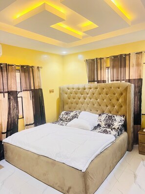 A bedroom with a tufted headboard, a bed with patterned bedding, and curtains with a striped design. - Modern & Clean 2 bedroom Apartment in Ipaja, 24/7 Power, Security & fast WiFi (Lagos)