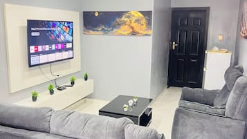 A modern living room with grey sofas, a flat-screen TV, a coffee table, and a painting on the wall.