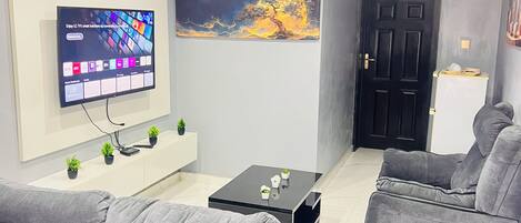 A modern living room with grey sofas, a flat-screen TV, a coffee table, and a painting on the wall.