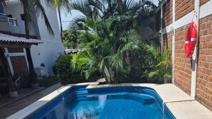 A swimming pool with clear blue water, surrounded by a brick wall and palm trees. - Perfect retreat 2 blks from beach in Villa Obregón neighbourhood  Melaque! (San Patricio)
