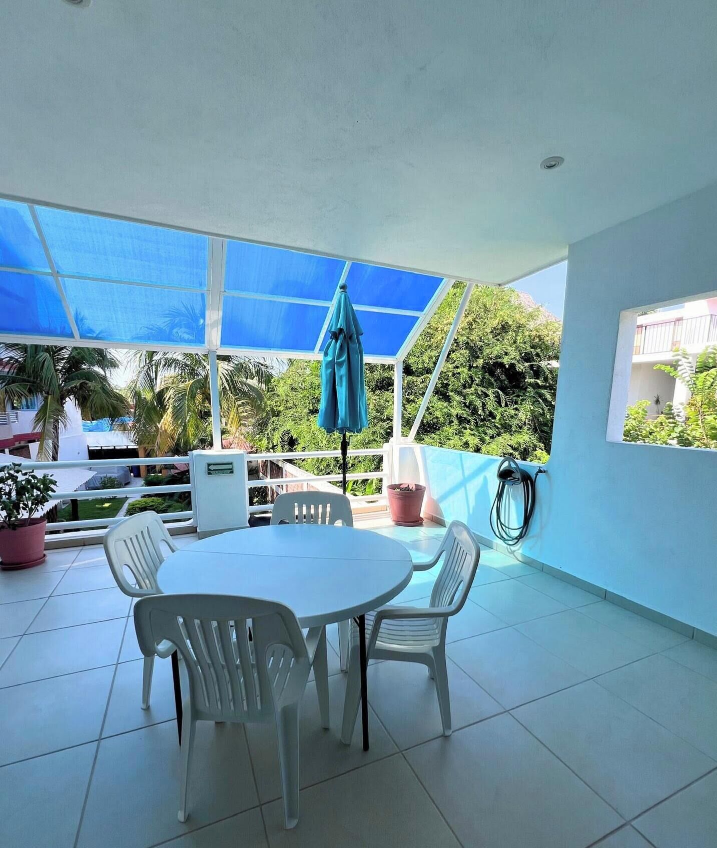Une terrasse couverte avec une table ronde et des chaises, un parasol bleu et une plante en pot.
