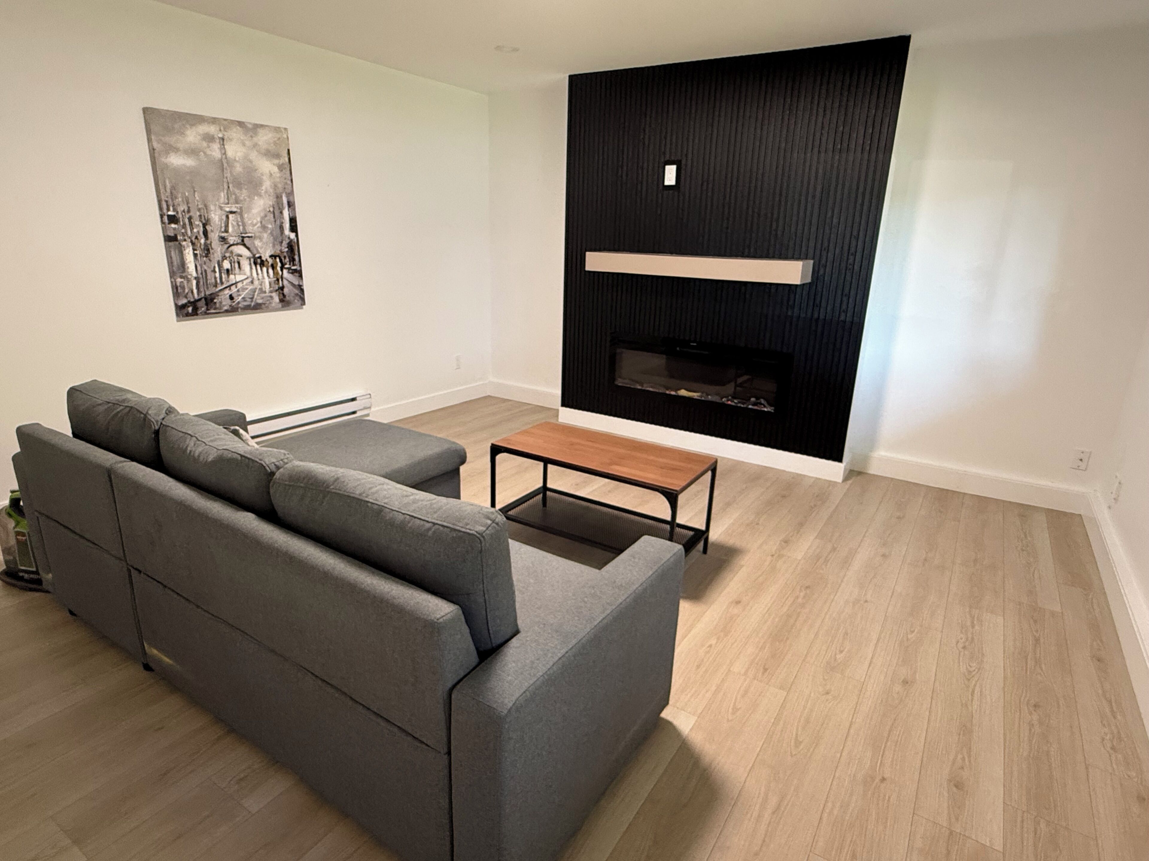 Una sala moderna con un sofá seccional gris, una mesa de centro de madera y una chimenea negra.