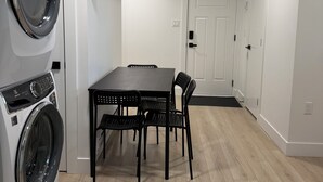 A laundry room with a washing machine, a table with chairs, and a door in the background. - Cozy home by YVR airport, Separated entrance, Free parking, Washer and dryer (Richmond)